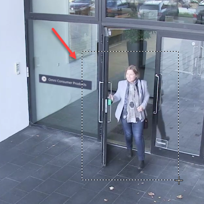 Camera feed of a person exiting a building. A dotted line around the person shows the zoom area.