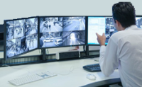 A person looking at two monitors. The monitors display XProtect Smart Client views.