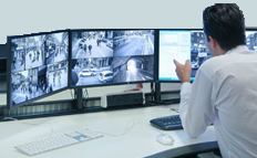 A person looking at three monitors. The monitors display XProtect Smart Client views.
